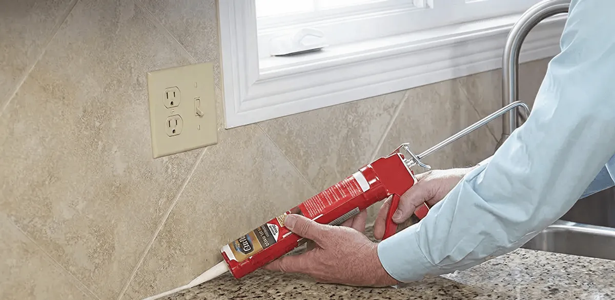 Handyman applying caulk along a kitchen backsplash and countertop seam in Newark, NJ